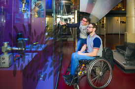 Frau und Mann im Rollstuhl vor Schaukasten im Museum