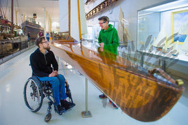 Mann im Rollstuhl und ältere Frau im Technischen Museum vor einem ausgestelltem Boot