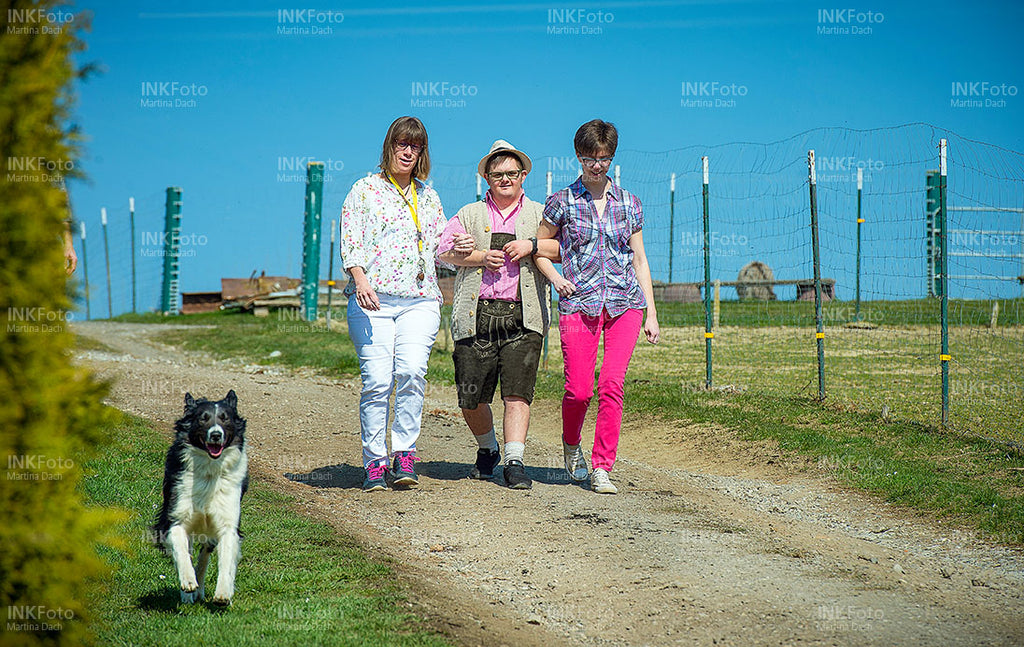 zwei Frauen und ein Mann wandern untergehakt auf dem Land