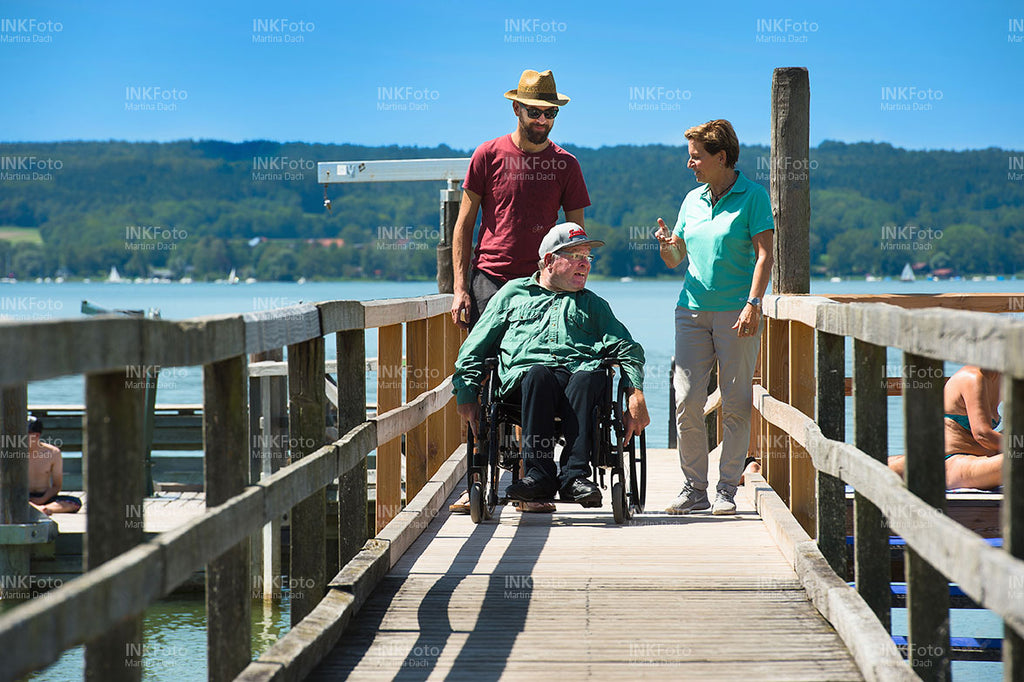 Mann im Rollstuhl am See unterhält sich mit einer Frau und einem Mann