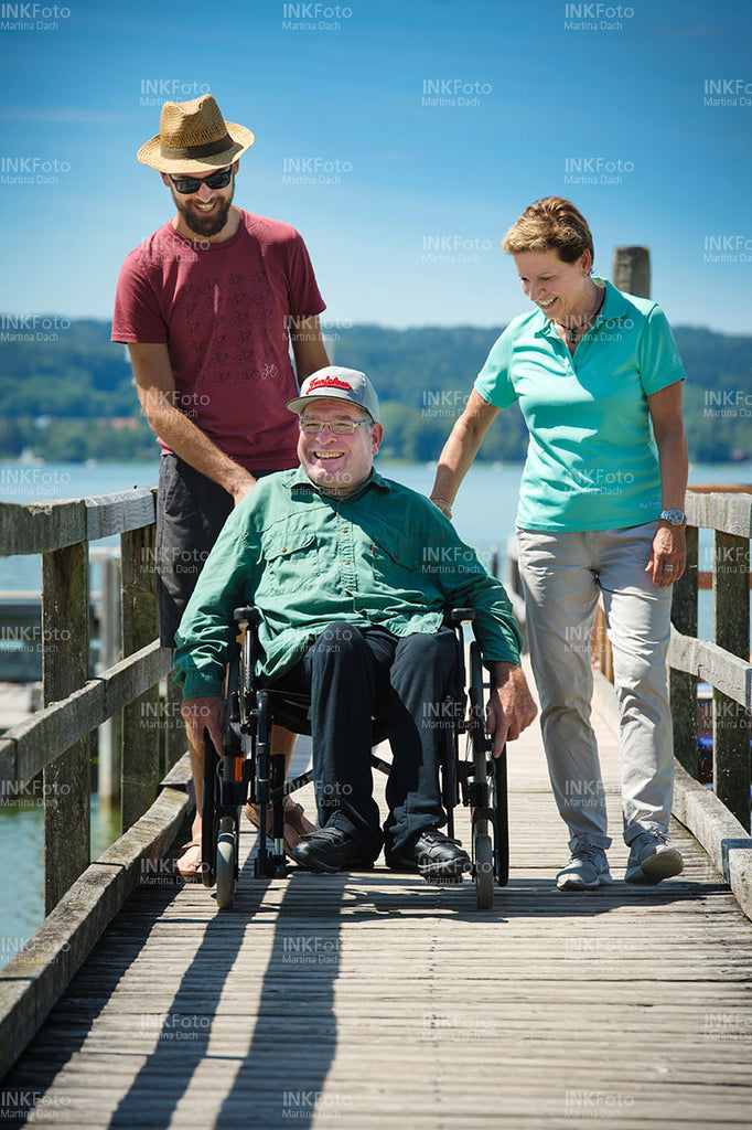 Mann im Rollstuhl am See unterhält sich mit einer Frau und einem Mann