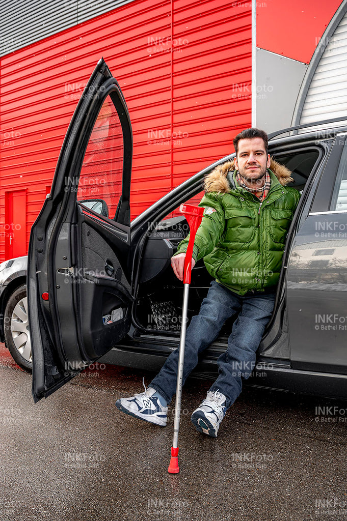 Junger Mann mit Krücken steigt aus dem Auto.