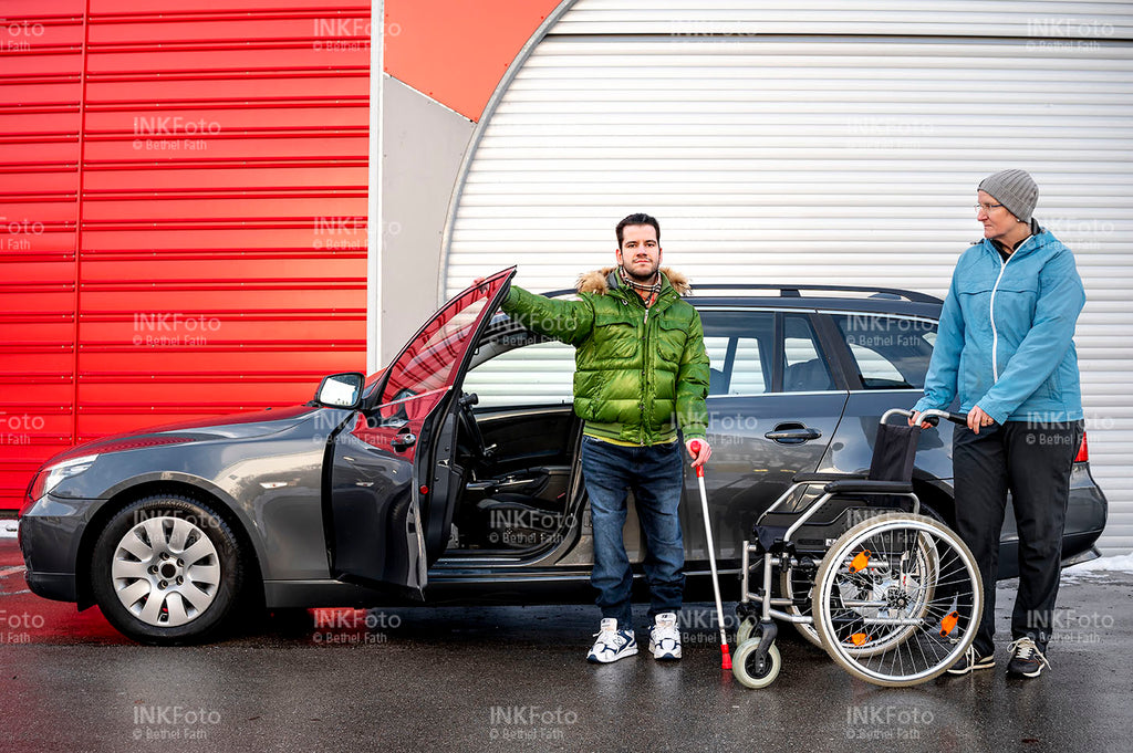Junger Mann mit Krücke und Rollstuhl vor einem Auto.