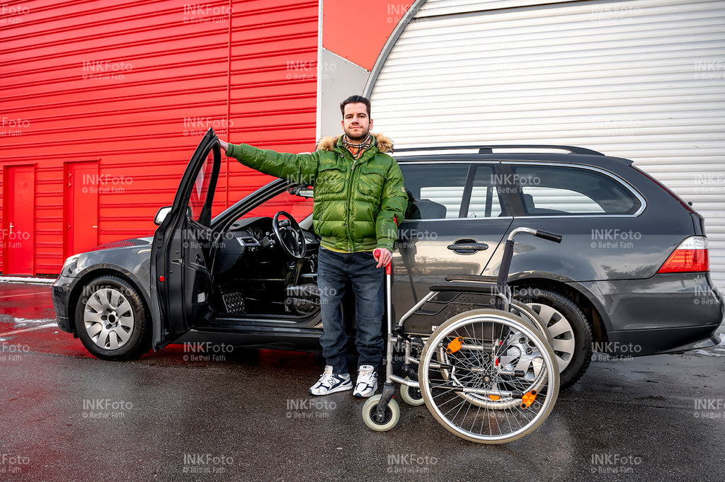 Junger Mann mit Krücke steht lässig vor einem Auto mit geöffneter Fahrertür.