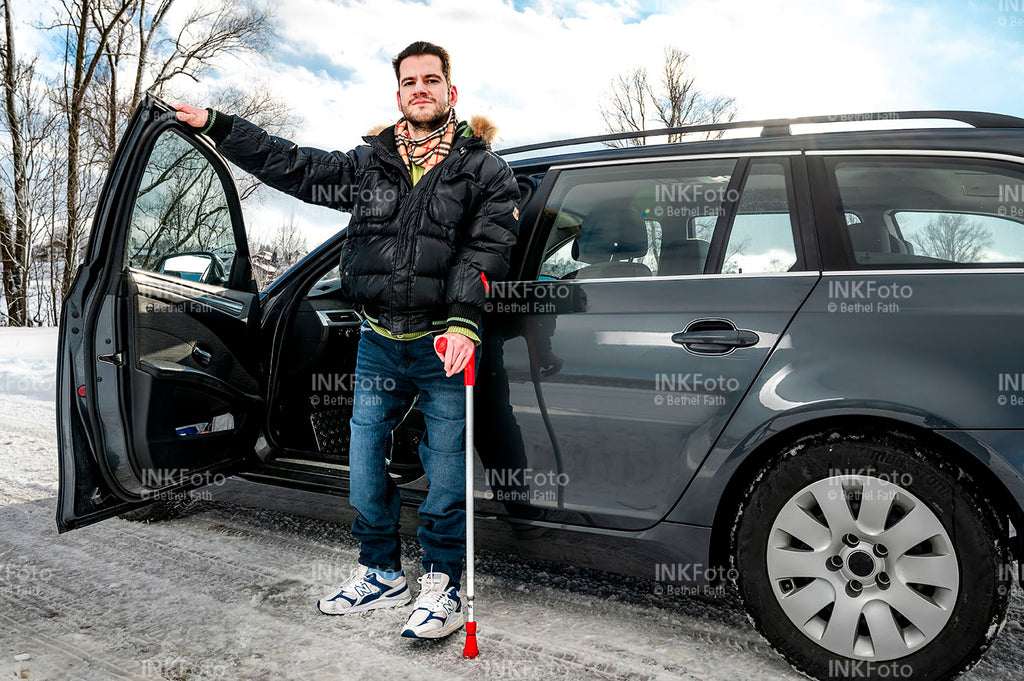 Junger Mann mit Krücke vor einem Auto.