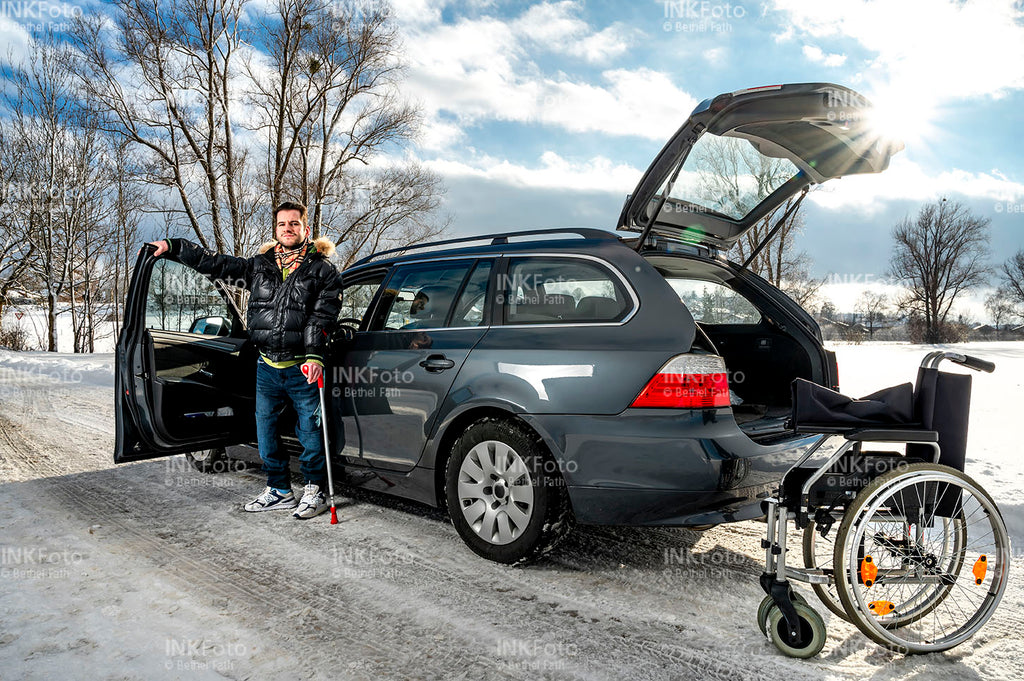 Junger Mann mit Krücke und Rollstuhl vor einem Auto.