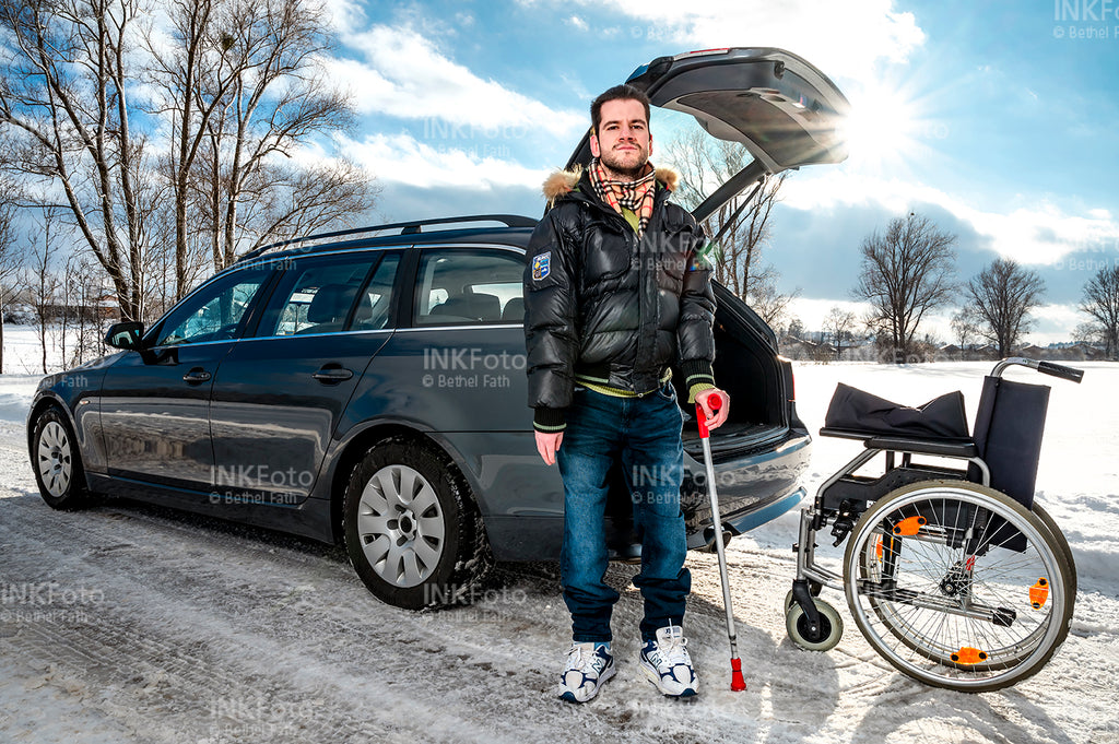 Junger Mann mit Krücke und Rollstuhl vor einem Auto.