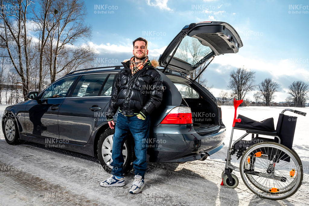 Junger Mann mit Krücke und Rollstuhl vor einem Auto.