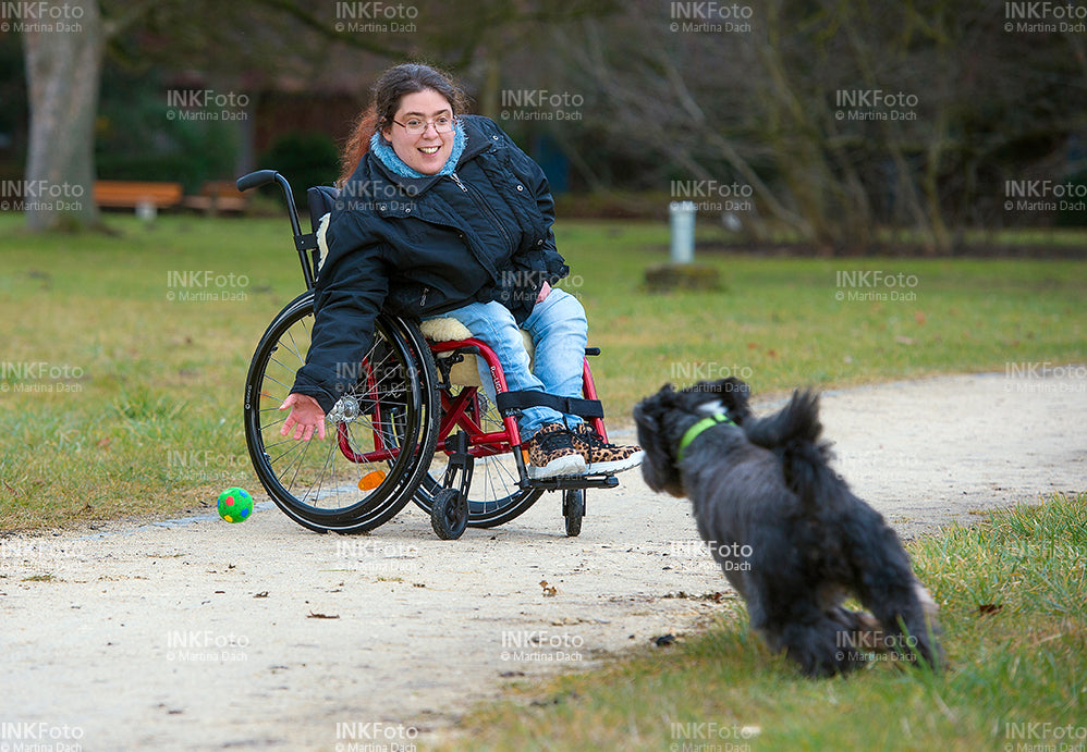 Junge Frau im Rollstuhl mit Hund im Park.