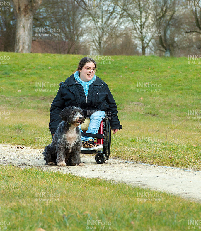 Junge Frau im Rollstuhl mit Hund im Park.