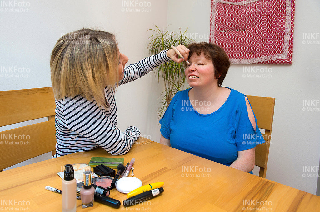 Visagistin schminkt Frau in mittleren Jahren.