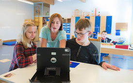 2 Jugendliche im Unterricht am Computer bei einer Lehrerin.