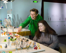 Frau im Rollstuhl mit Begleiterin im Glas-Museum