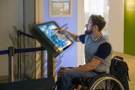 Junger Mann im Rollstuhl bedient eine interaktive Schautafel in einem Museum