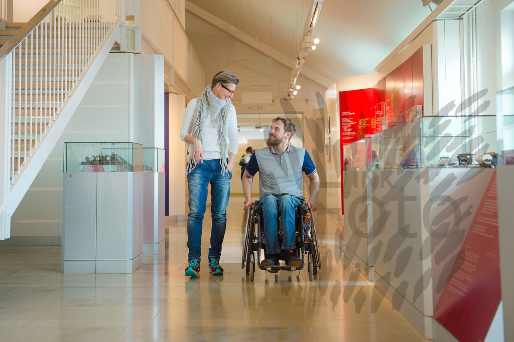 Mann im Rollstuhl mit Frau gehen durch ein Museum