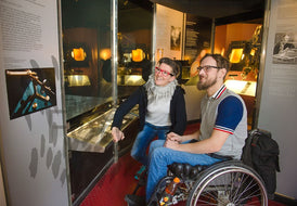 Frau und Mann im Rollstuhl vor Schautafel im Museum