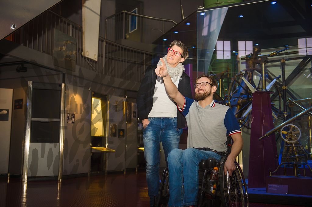 Junger Mann im Rollstuhl und Frau im mittleren Alter in einem technischen Museum
