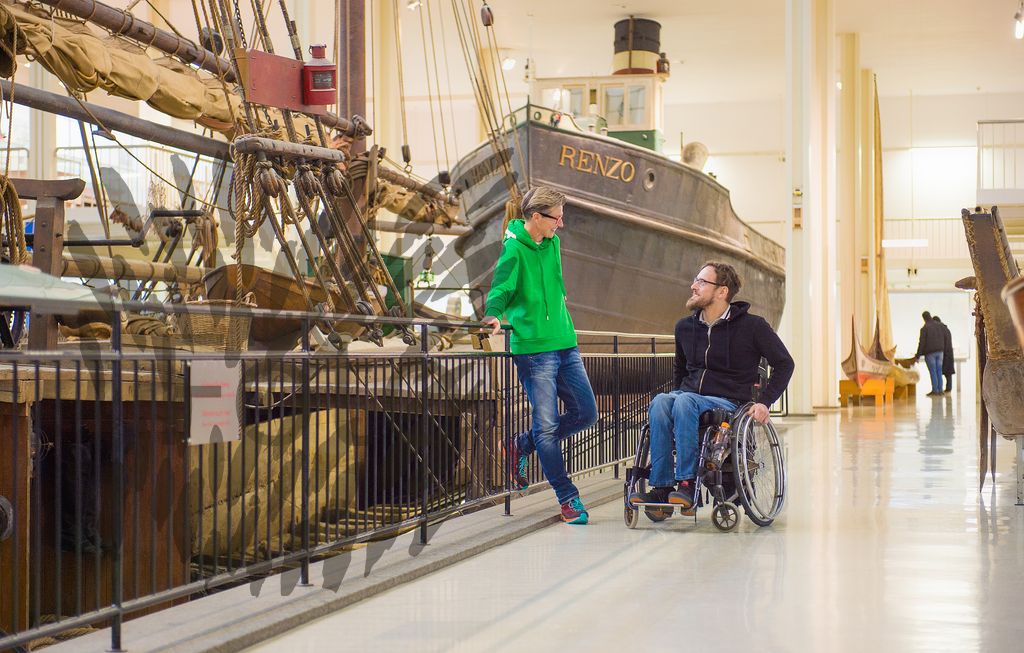 Mann im Rollstuhl und ältere Frau im Technischen Museum vor einem ausgestelltem Boot