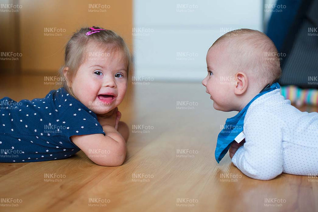Baby und Kleinkind mit Behinderung liegen lachend am Boden