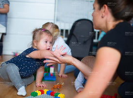 Mutter spielt mit Kleinkindern mit und ohne Behinderung mit Lego