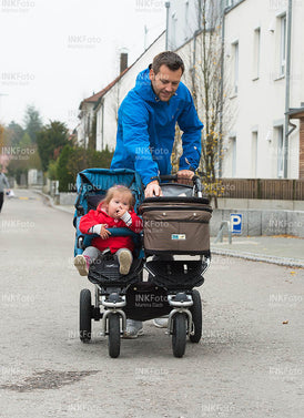 Junger Vater mit Kinderwagen und zwei Kindern mit und ohne Behinderung