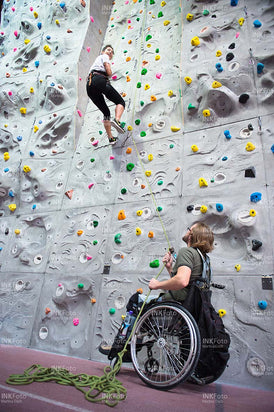 Junger Mann im Rollstuhl sichert Frau an der Kletterwand