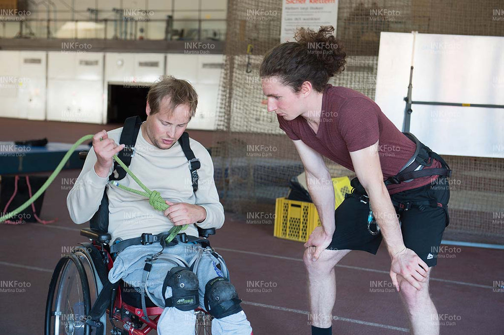 Junger Mann im Rollstuhl erhält Unterricht im Klettern von einem Lehrer