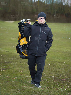 Junger Mann mit Behinderung auf dem Golfplatz in warmer Kleidung