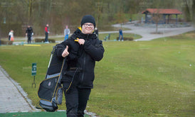 Junger Mann mit Behinderung auf dem Golfplatz mit Golfbag und warmer Kleidung