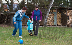 Zwei Frauen und ein Kleinkind spielen Ball im Garten.