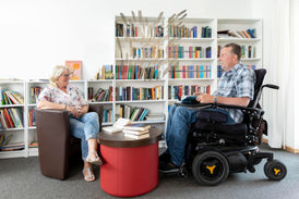 Mann im Rollstuhl mit Ehefrau in einer Bibliothek