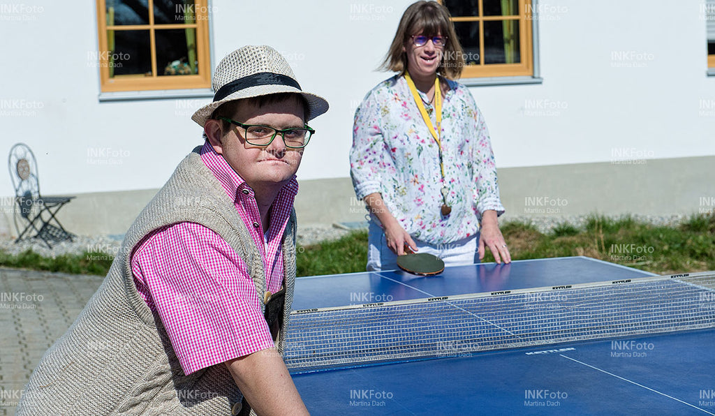 Ein Mann und eine Frau beim Tischtennis spielen vor einem Bauernhof.