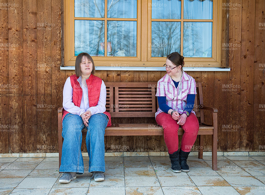Zwei junge Frauen sitzen auf einer Bank vor einem Bauernhof.