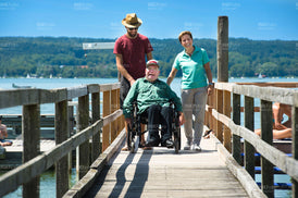 Mann im Rollstuhl am See unterhält sich mit einer Frau und einem Mann