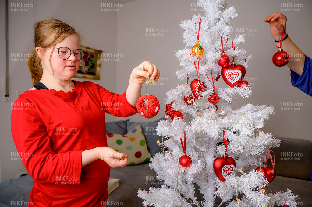Junges Mädchen mit rotem Pullover schmückt einen Weihnachtsbaum mit Kugeln.
