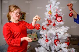 Junges Mädchen mit rotem Pullover schmückt einen Weihnachtsbaum mit Kugeln.