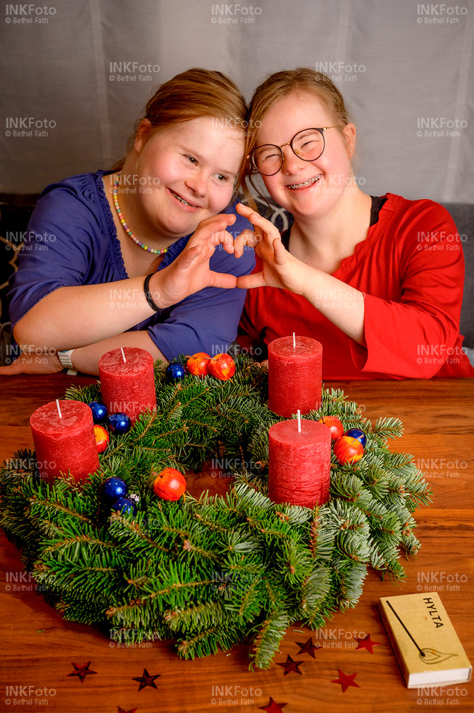 Zwei junge Mädchen sitzen vor einem fertig geschmückten Adventskranz