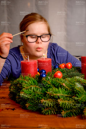 Junges Mädchen zündet mit einem Streichholz eine Kerze am Adventskranz an.