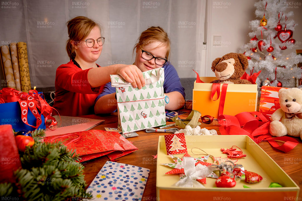 2 junge Mädchen sitzen an einem großen Holztisch und packen Geschenke ein.