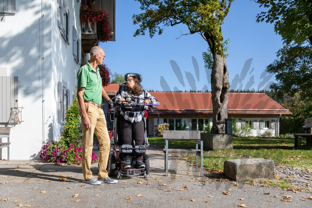Ein Mann und eine junge Frau im Rollstuhl unterhalten sich.
