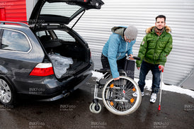 Junger Mann mit Krücke und Rollstuhl vor einem Auto.
