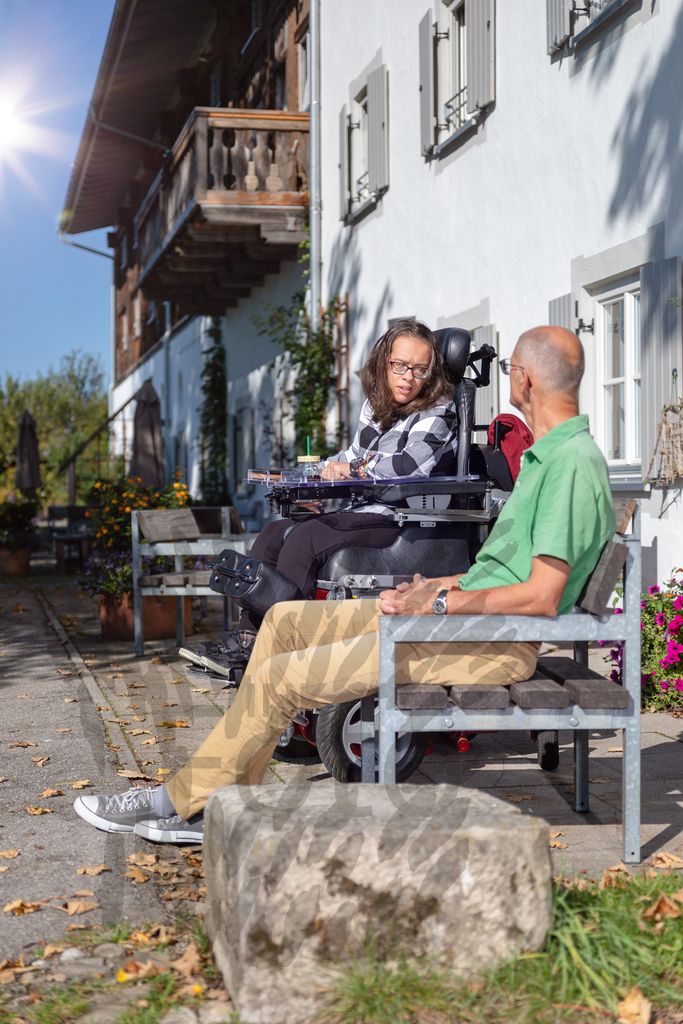 Junge Frau im Rollstuhl unterhält sich mit älteren Mann vor einem Haus