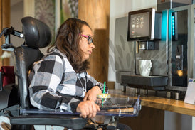 Junge Frau im Rollstuhl bedient eine Kaffeemaschine