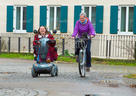 2 Frauen unterwegs in der Stadt mit Scooter und Fahrrad