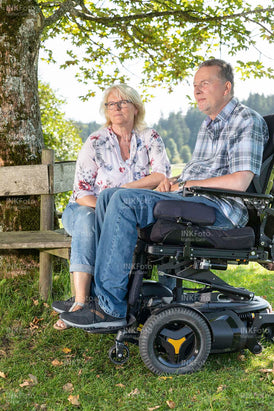Ehepaar im Rollstuhl sitzt entspannt im Garten und genießt die Atmosphäre