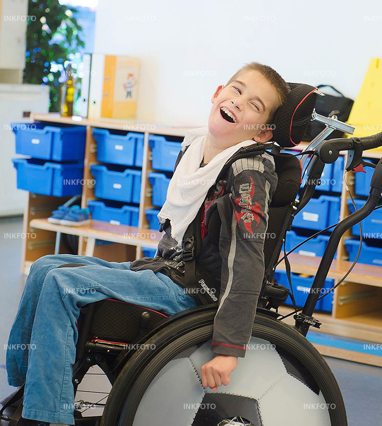 Lachender Junge in der Schule im Rollstuhl.