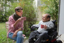 Mann im Rollstuhl mit Frau im Garten beim Kaffeetrinken