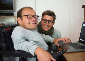 Mann im Rollstuhl mit Frau am Arbeitsplatz im Homeoffice