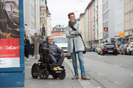 Mann im Rollstuhl mit Frau in der Stadt an einer Bushaltestelle