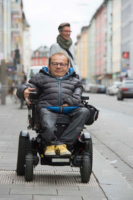 Mann im Rollstuhl mit Frau in der Stadt an einer Bushaltestelle